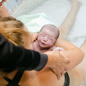 A woman in a pool holds her newborn baby