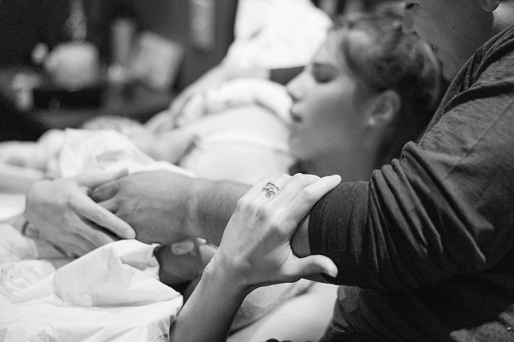 A woman and man smile down at her newborn baby